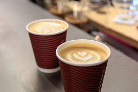 Side view of two latte art coffees with heart figure on, in take away paper glass in a cafe.の写真素材