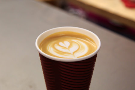 Side view of latte art coffee with heart figure on, in take away paper glass in a cafe.の写真素材