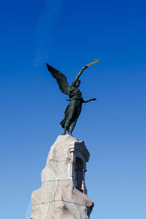 Angel woman sculpture on a rock with a cross holding on hand, on navy blue sky background.の写真素材