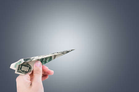 Flying paper plane with dollar banknote holding in hand, on grey background.の写真素材