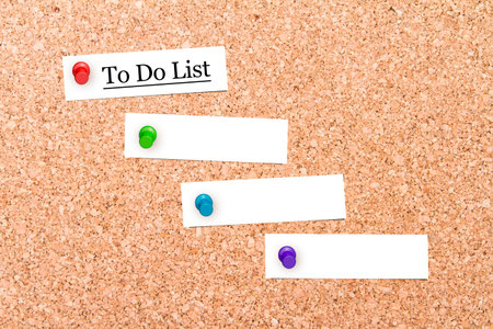 Close up front view of illustrative corkboard with to do list text on blank white note cards pinned,...