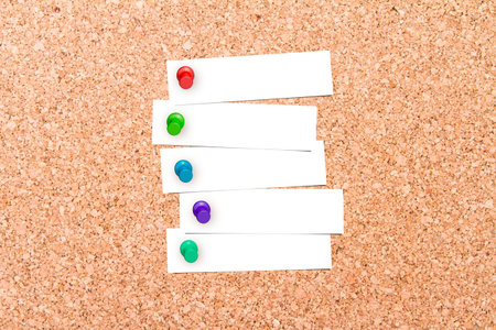 Close up front view of illustrative corkboard with blank white note cards pinned with colorful pins,...