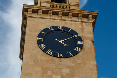 View of a church in Valletta Malta with limestone belfry clock tower, on cloudy blue sky background.の写真素材