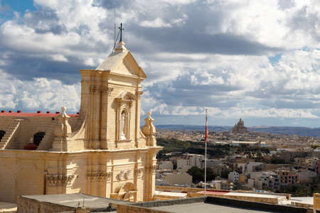 View of a historical church in Victoria, Malta with a limestone belltower, on cloudy sky background.の写真素材