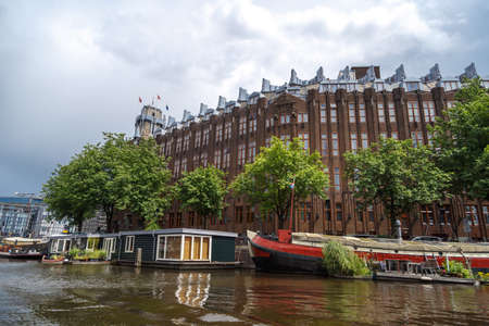 AMSTERDAM, NETHERLANDS - JULY 2, 2016 : View of typical Amsterdam houses along canal on cloudy sky. Sailboats have tours on Amsterdam canals.のeditorial素材