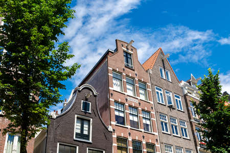 AMSTERDAM, NETHERLANDS - JULY 2, 2016 : View of typical Amsterdam houses with sharp roofs on bright blue sky. Amsterdam is famous with its architecture.のeditorial素材