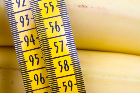 Close up detailed view of yellow tape measure with banana, health and fit life concept on wooden...