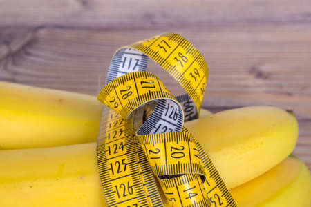 Close up detailed view of yellow tape measure with banana, health and fit life concept on wooden background.の写真素材