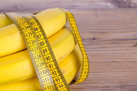 Close up detailed view of yellow tape measure with banana, health and fit life concept on wooden background.の写真素材