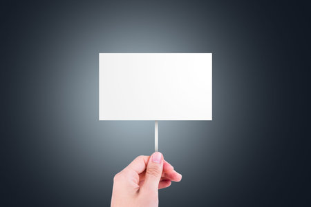 Single hand holding blank, white cardboard with copy space for design, on dark background.