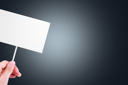 Single hand holding blank, white cardboard with copy space for design, on dark background.の写真素材