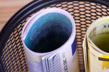 Bankroll cash euro banknotes in garbage basket focused on consuming in finance concept on wooden background.の写真素材