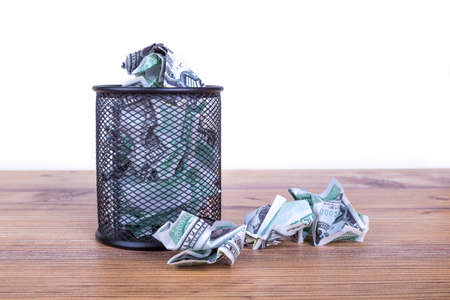 Dollar banknotes crumpled inside garbage basket, rubbish bin focused on consuming money in finance concept, isolated on white background.の写真素材