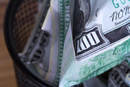 Dollar banknotes crumpled inside garbage basket, rubbish bin focused on consuming money in finance concept, on wooden background.の写真素材