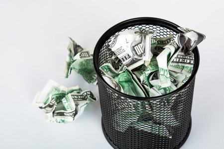 Dollar banknotes crumpled inside garbage basket, rubbish bin focused on consuming money in finance concept, isolated on white background.の写真素材