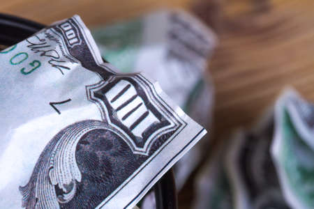 Dollar banknotes crumpled inside garbage basket, rubbish bin focused on consuming money in finance concept, on wooden background.の写真素材