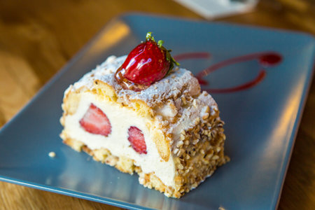 Close up detailed view of slice of cream cake with strawberry and nuts on wooden background.の写真素材