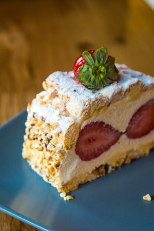 Close up detailed view of slice of cream cake with strawberry and nuts on wooden background.