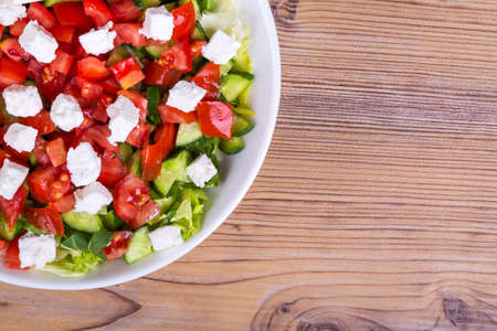 Bowl of healthy green salad with tomato and white cheese on wooden background.の写真素材