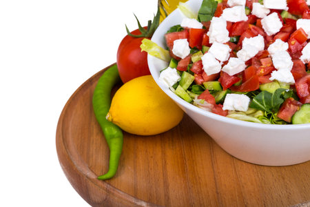 Bowl of healthy green salad with tomato and white cheese, served on wooden plate with vegetables and olive oil, isolated on white background.の写真素材