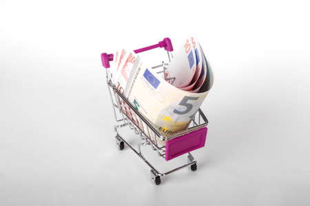 Stack of Euro banknotes in shopping cart with money consuming and finance, isolated on white background.の写真素材