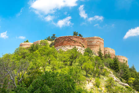 Historical Kutahya Castle with brick stone walls and bastions, at the hill surrounded with trees, on cloudy blue sky background.の写真素材