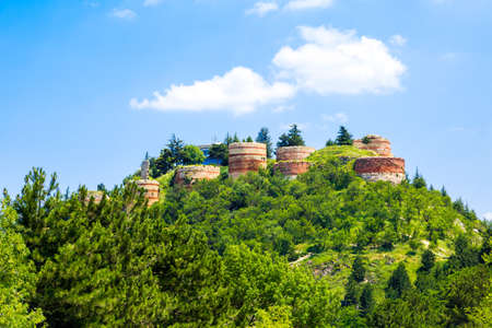 Historical Kutahya Castle with brick stone walls and bastions, at the hill surrounded with trees, on cloudy blue sky background.の写真素材