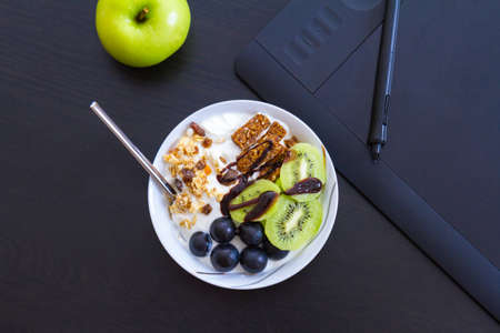 Top view of graphic design and healthy lifestyle concept, close up view of cup with raw bars and grape, kiwi fruits inside. Tablet and green apple behind.の写真素材