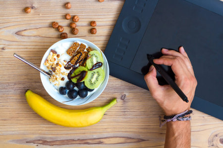 Graphic design and healthy lifestyle concept, top view of cup with raw bars and grape, kiwi fruits inside. Tablet and green apple behind on wooden table.の写真素材
