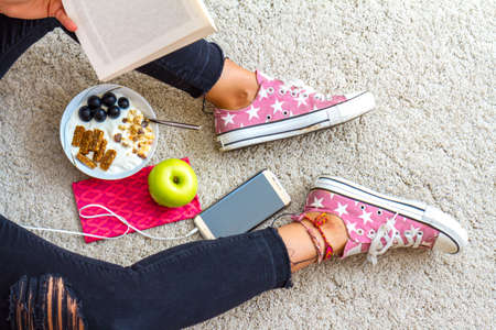 Close up view of casual style woman legs with healthy eating concept with apple, yogurt and some fruits with phone and book.の写真素材