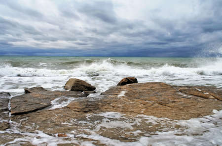 Ocean scape with waves breaking on a rocky coastline under an overcast stormy sky. Caspian Sea.の写真素材