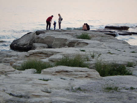 People walk along the evening seashore. Rocky shore of the Caspian Sea. Aktau city. Kazakhstan. 26 of May. 2019 year.のeditorial素材