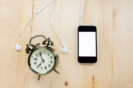 Retro alarm clock with mobile phone on wooden table.の写真素材