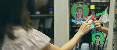 iot smart retail futuristic technology concept, happy girl try to use smart display with virtual or augmented reality in shop or retail to predict select color of new hair by artificial intelligenceの写真素材