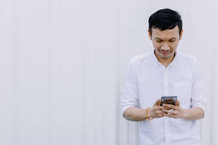 Asian man using a mobile phone smile with white walls.の写真素材