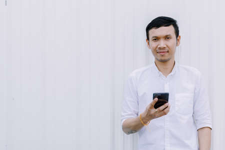 Asian man using a mobile phone smile with white walls.の写真素材
