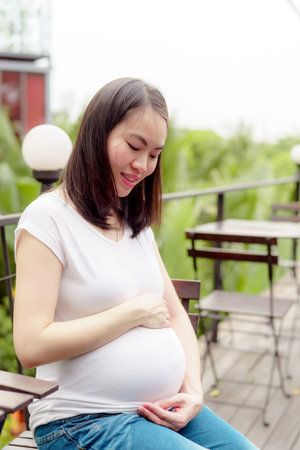 A pretty Asian woman is pregnant. Wearing a white shirt Sit back and relax in the balcony of the...