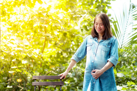 A pretty Asian woman is pregnant. Wearing a denim shirt Sit and relax in the garden