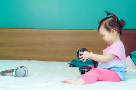 A little girl sitting listening to a big headset In the bed in the bedroom happilyの写真素材
