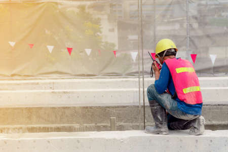 The construction worker in the red waistcoat and yellow helmet and the rubber boots with the red radio communication in the hand are working in the construction area.の写真素材
