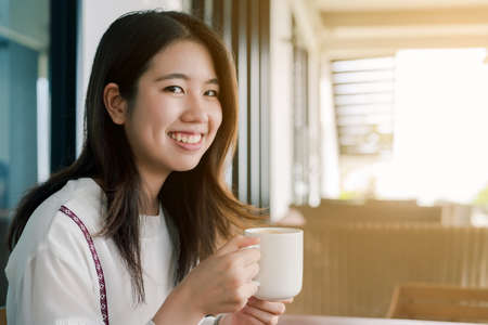Asian beautiful woman Wearing a white shirt, sitting, drinking hot coffee In the bakery Happily bright in the morning.の写真素材