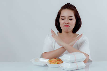 Beautiful Asian woman, white shirt Sitting in front of the dining table There is an expression of disgust in the foam box. Do not support using food foam Placed in front With a white background.の写真素材