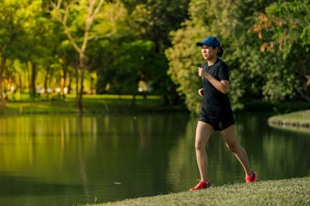 Asian middle-aged woman wearing a black dress, blue hat, running stretching in park near to lake. Get the sun light in the morningの写真素材