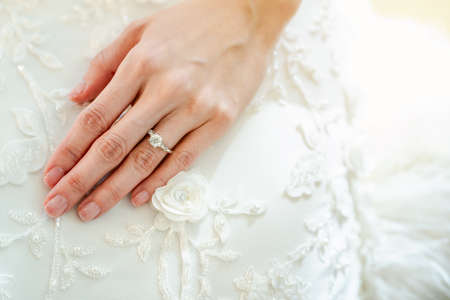 The close-up of the girl's hand is wearing a ring on the left ring finger. Put your hands on the white bridal gown.の写真素材
