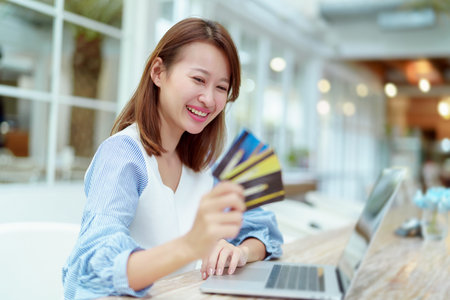 A beautiful Asian woman in a white shirt is sitting in front of a computer with a credit card in her...