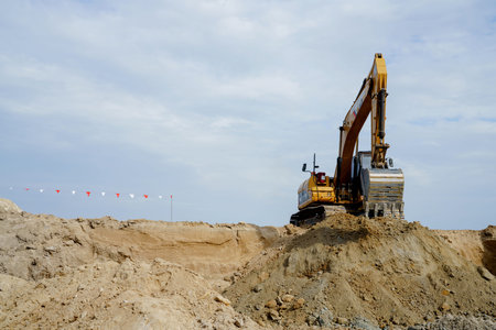 A large yellow backhoe is planting and grading brown rays in a factory construction area.