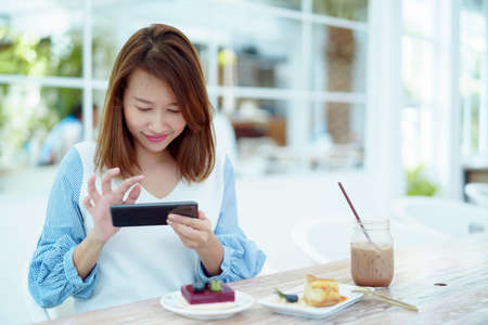 Portrait A beautiful, white Asian woman in a white shirt is happily sitting on her phone in a bakery.の写真素材