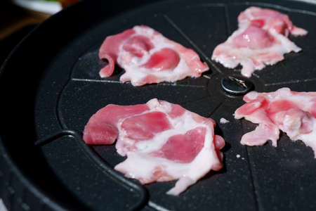 Sliced raw pork into thin slices is placed on a black grill to cook before eating.の写真素材