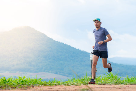 Asian male runners in blue shirts, sportswear and hats are practicing running on a dirt road behind...