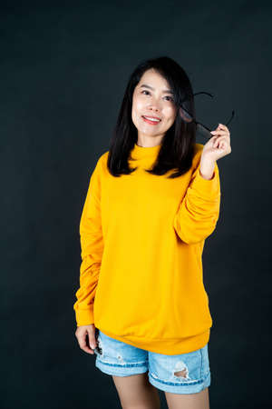 Portrait of an Asian woman wearing a yellow shirt against a black background smiling happily in the studio looking at the camera.の写真素材